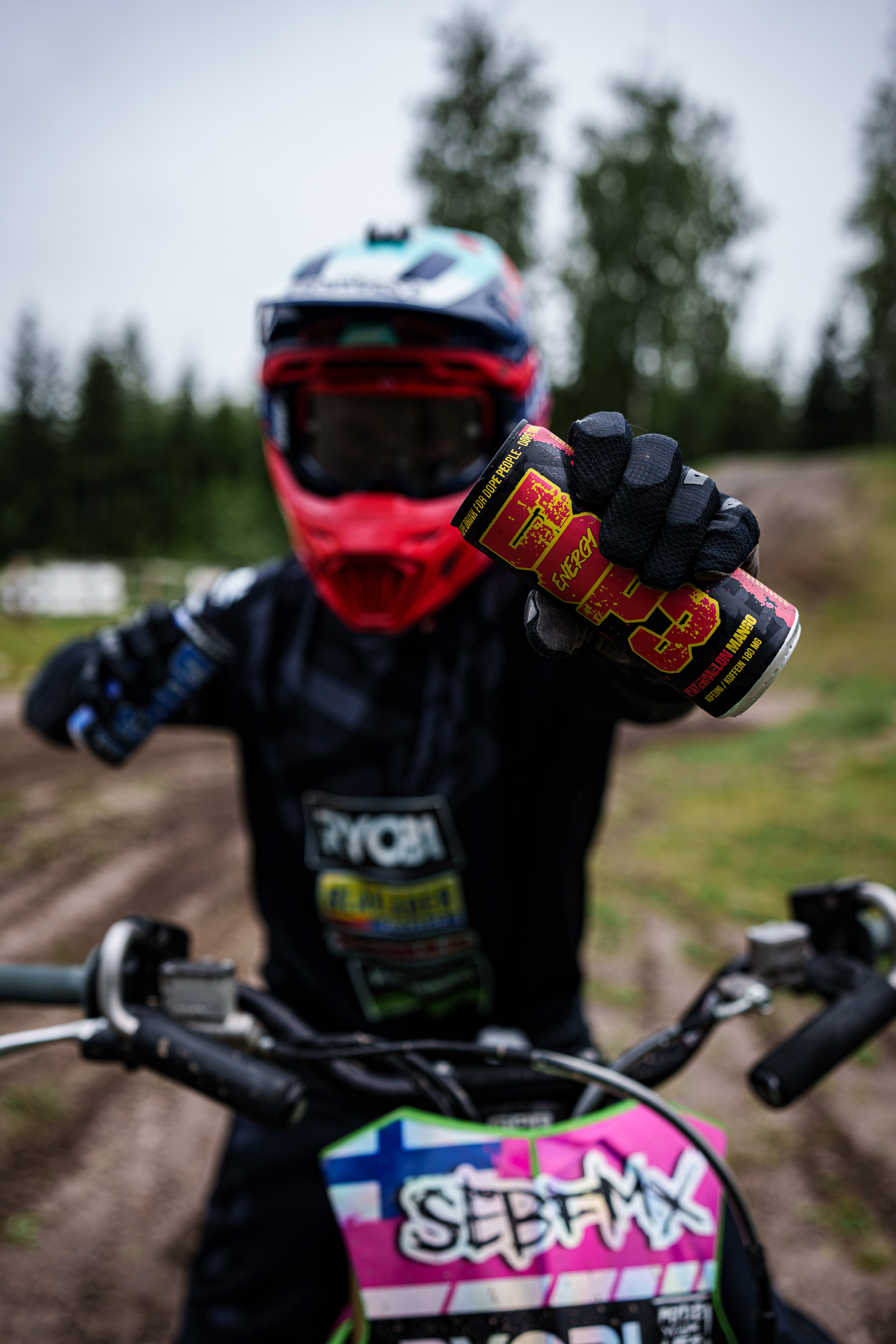 Motocross rider holding a DOP3 Energy can in front of the camera while sitting on a dirt bike